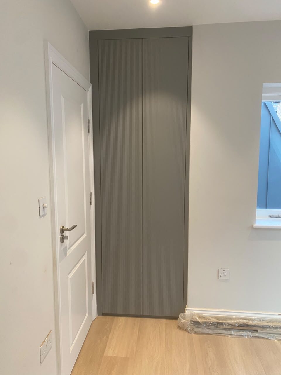Two-door grey fluted fitted wardrobe running floor to ceiling beside a doorway