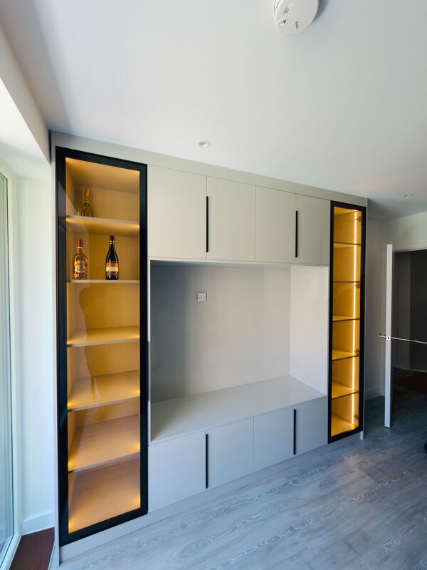 Living room media wall with lit black-framed glass display cabinets either side of a television recess and drawers below