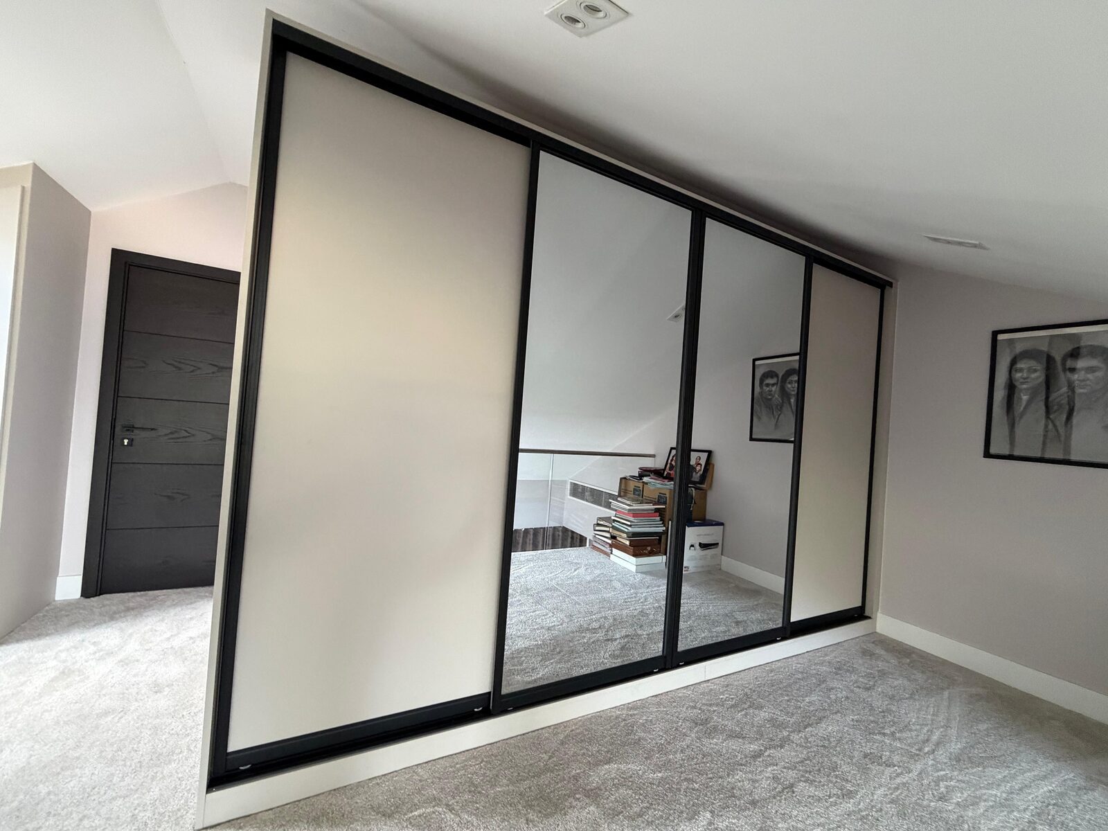 Four sliding wardrobe doors with black frames, alternating cream and mirrored panels, with the top track following a sloping ceiling