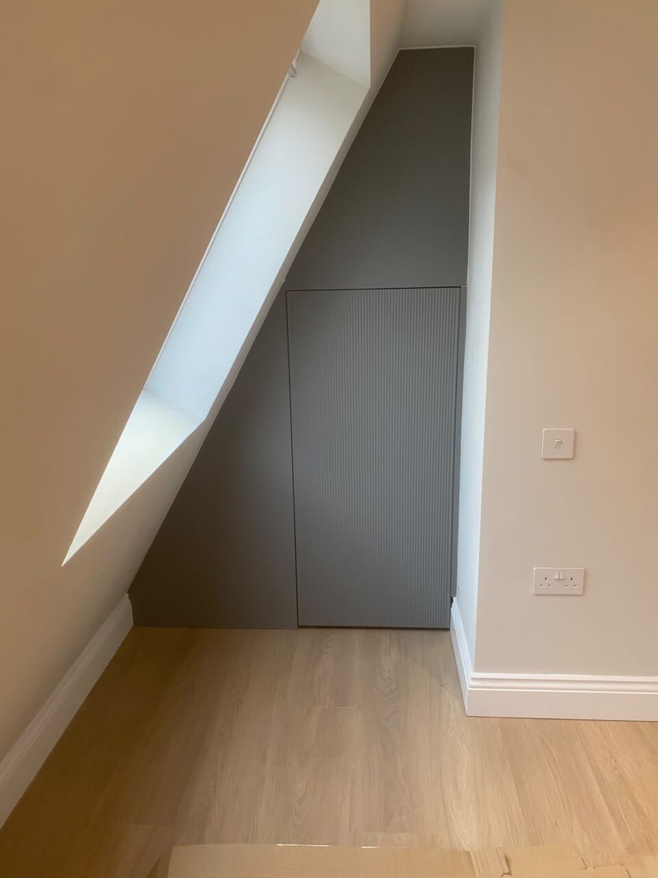 Grey fluted wardrobe door fitted into a triangular under-stairs space, handleless push-to-open