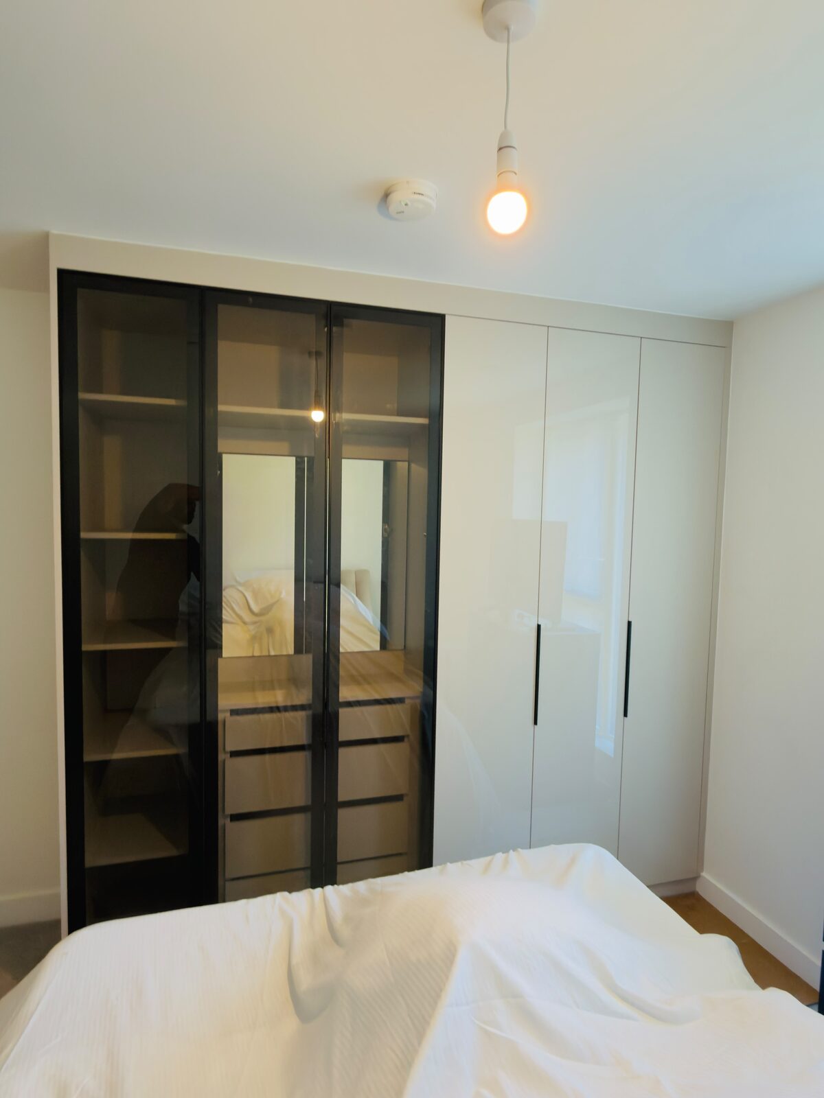 Fitted wardrobe by UKB with black-framed glass and mirrored doors alongside high-gloss white hinged doors, internal drawers visible through the glass